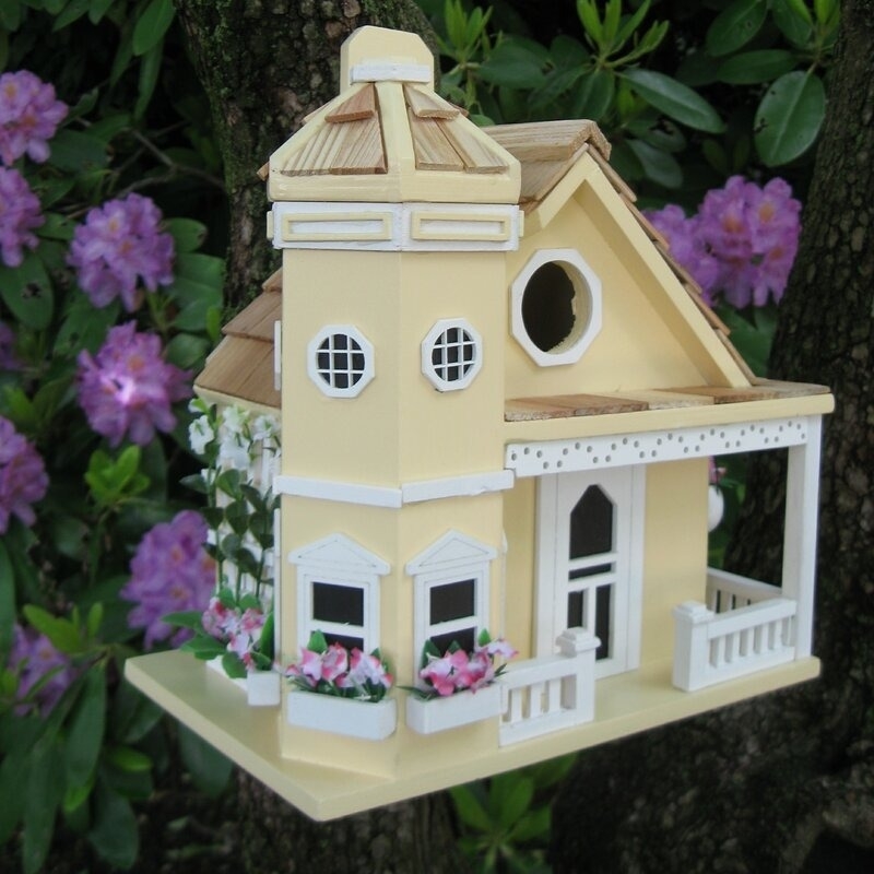 Birdhouse resembling a miniature Victorian-style house with decorative trim and flowers