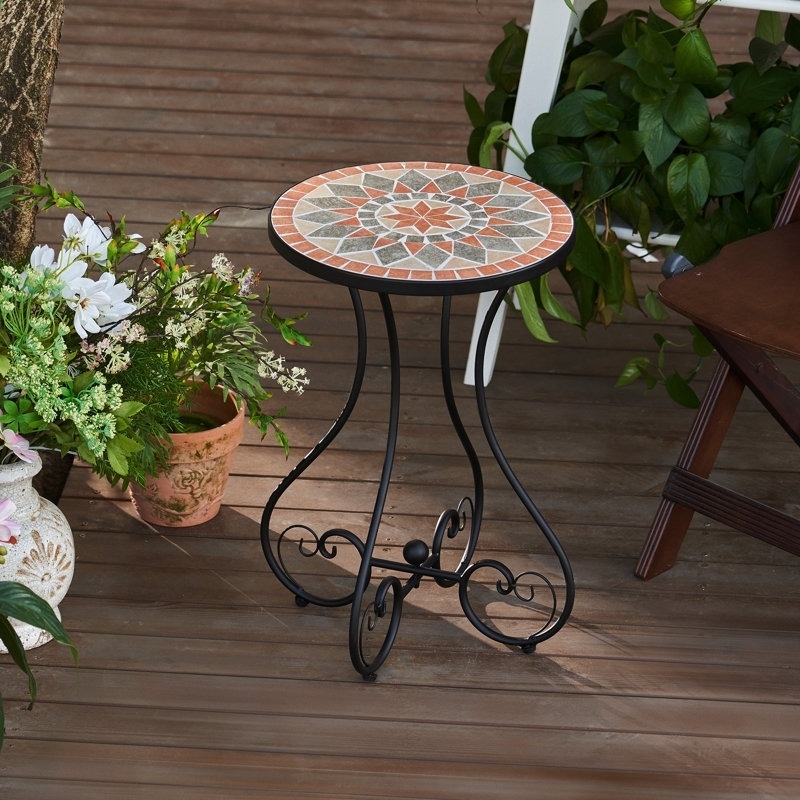 Mosaic-tiled round table with wrought-iron legs, placed on a wooden deck next to plants