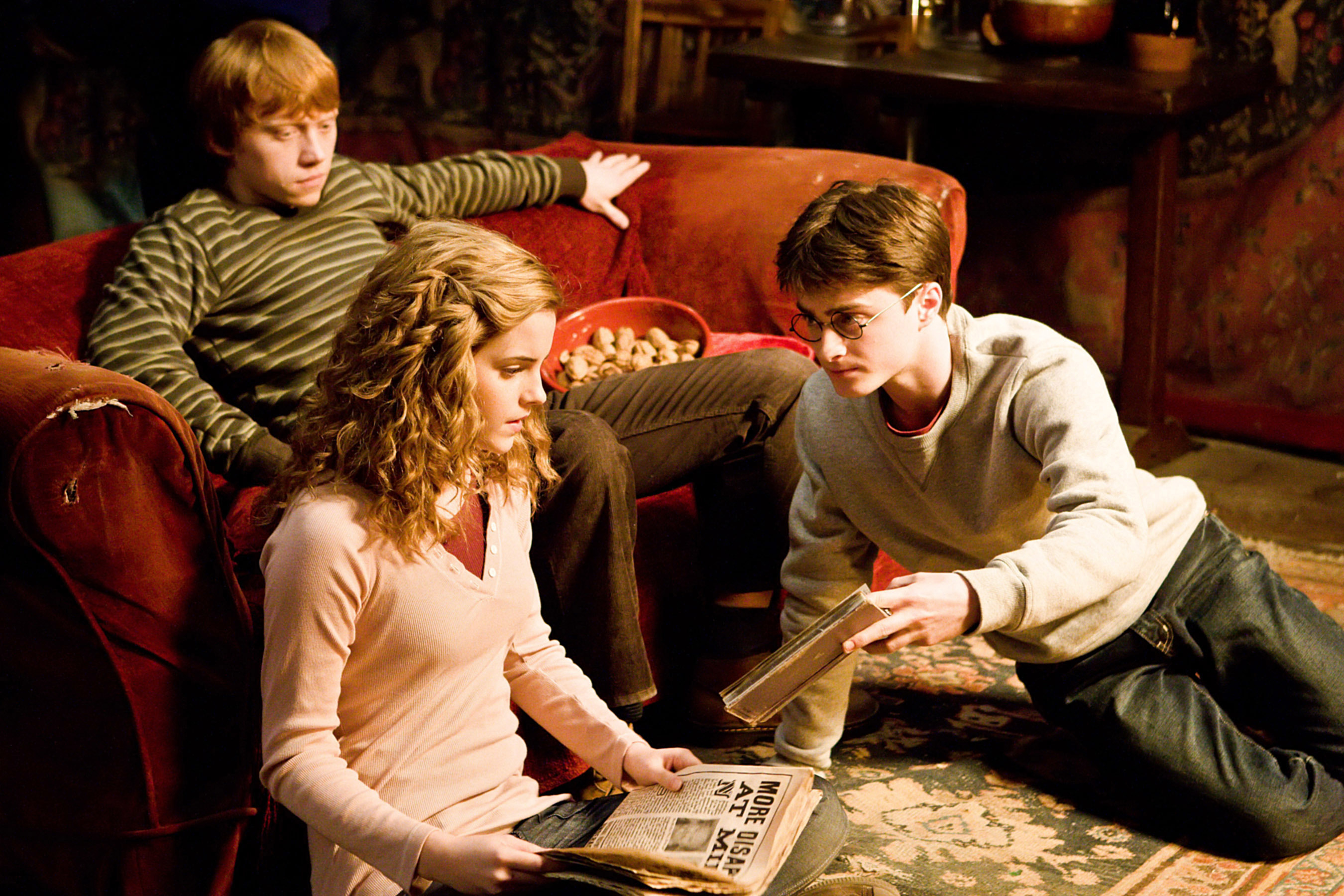 Characters Hermione Granger, Ron Weasley, and Harry Potter sitting with a newspaper in a scene from a film