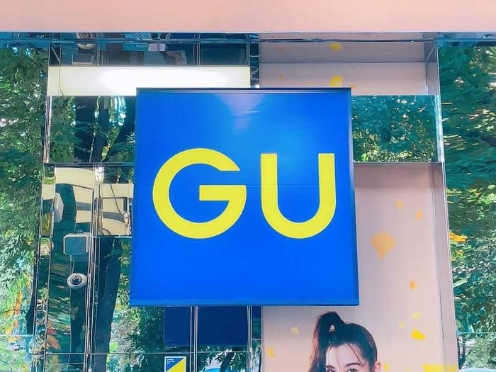 Sign for "GU" store with portion of a person's face in the bottom corner