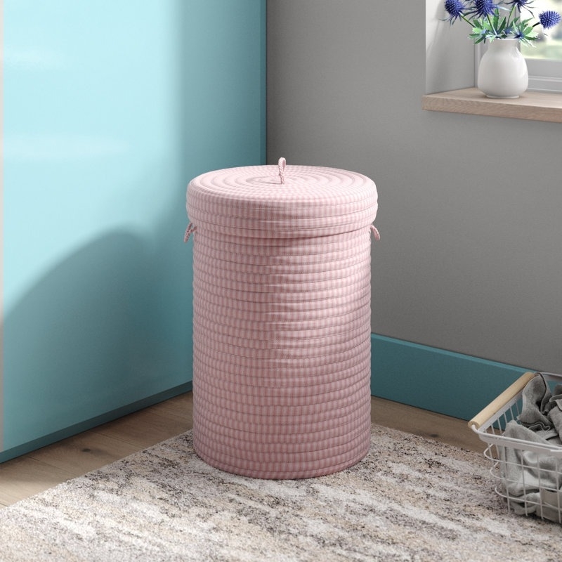 Pink woven laundry basket with lid in a room next to a pile of clothes