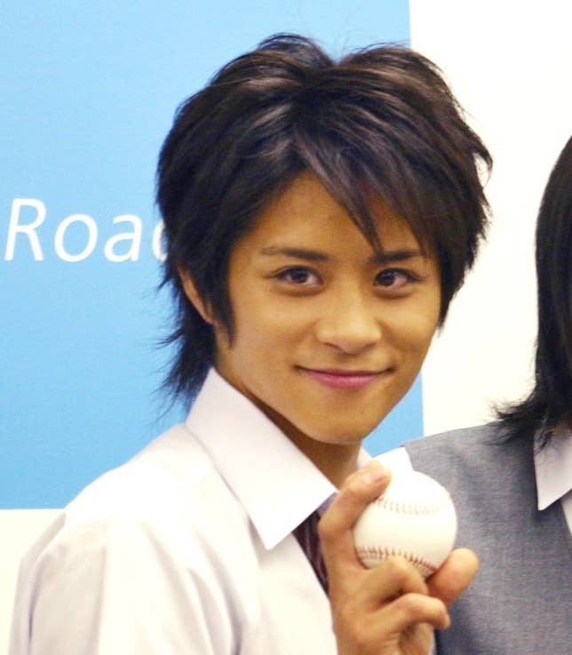 白シャツに黒髪の若い男性が笑顔で野球ボールを持っている。