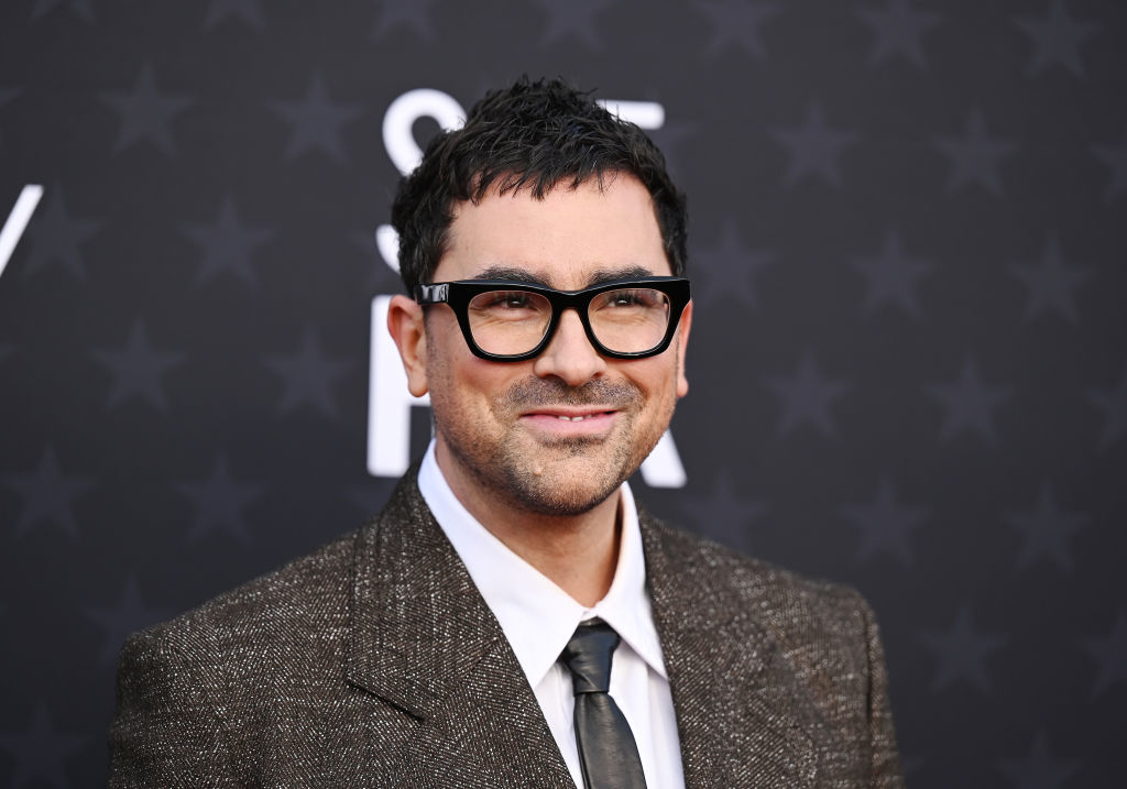 Dan Levy wearing glasses, smiling in a textured suit with a tie at an event