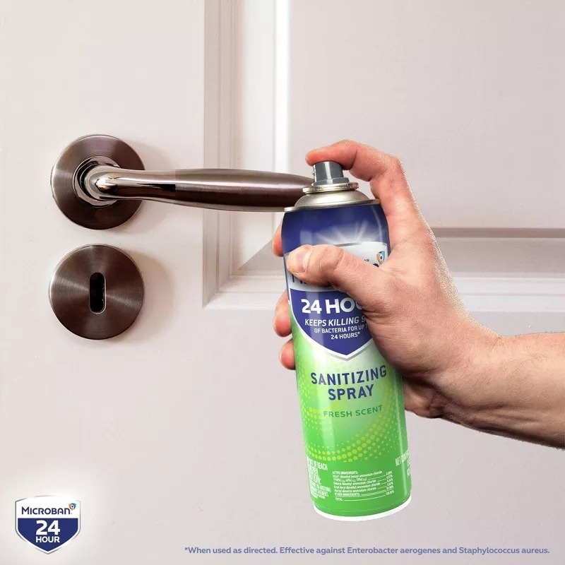 Hand holding a can of Microban 24 Hour sanitizing spray, aiming it at a door handle