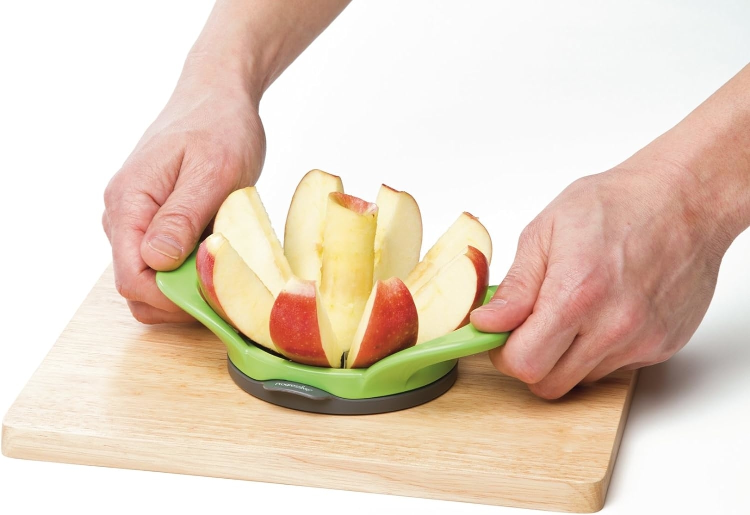 Hands using an apple slicer on a cutting board to cut an apple into wedges