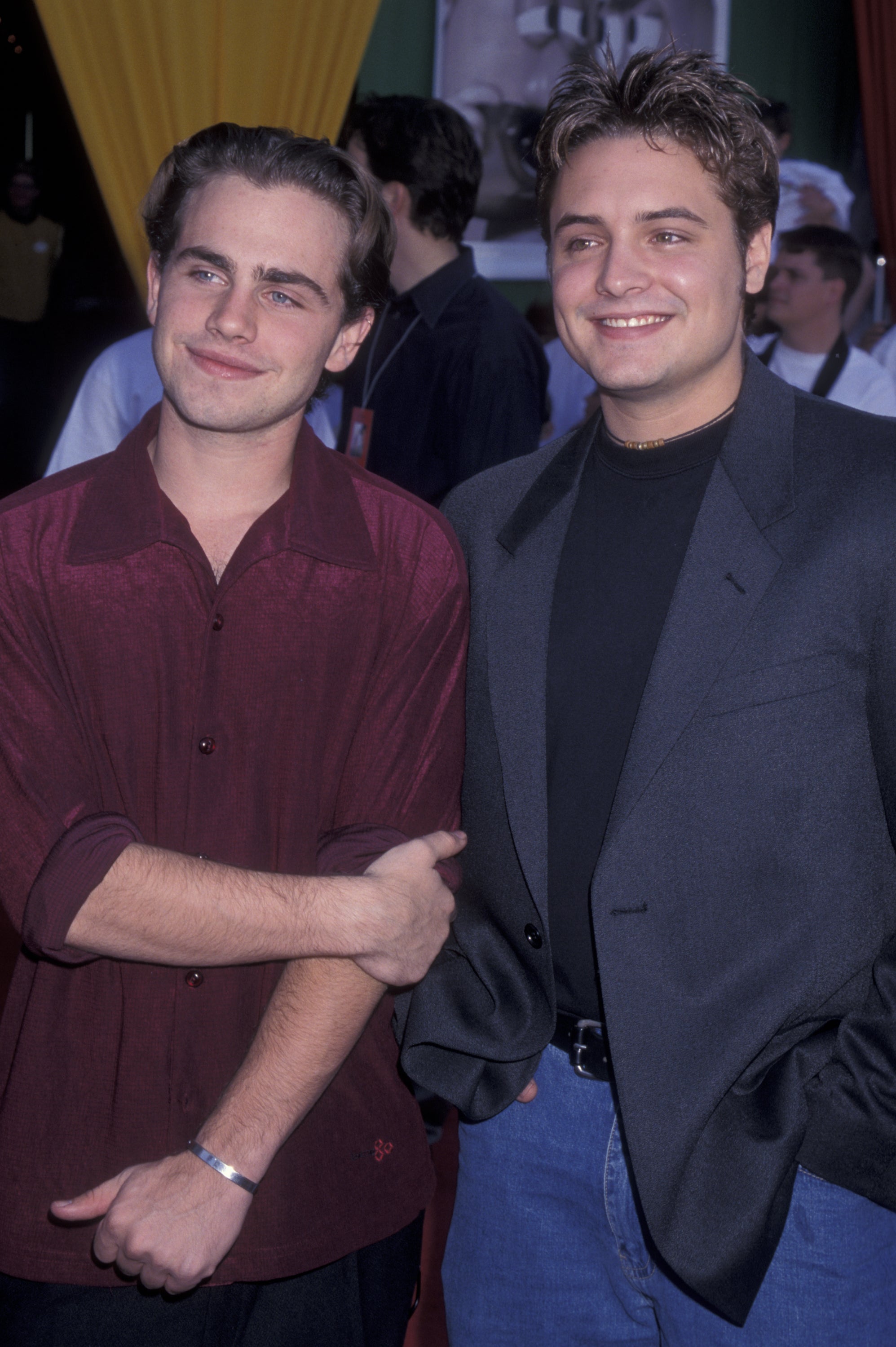 Two people standing side by side, one in a red shirt and the other in a black shirt with a blazer