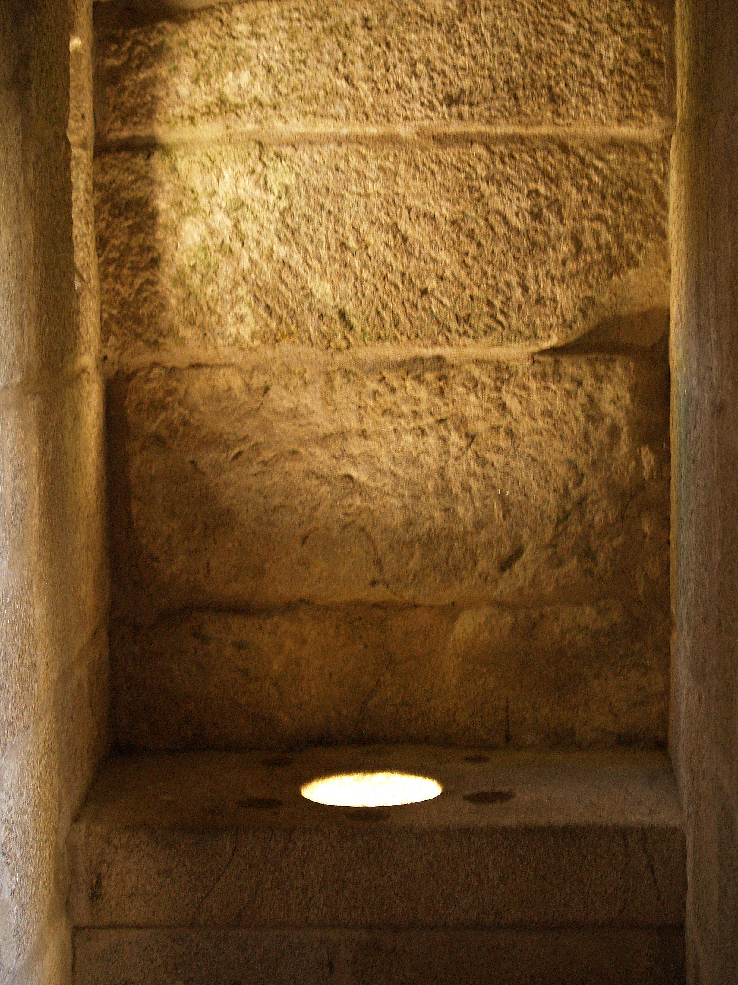 Stone chamber with a circular opening on the floor allowing light into the dark interior
