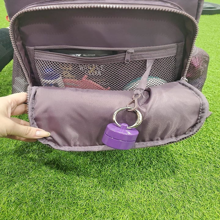 A reviewer's hand holding open travel bag with an attached purple collapsible lion latch