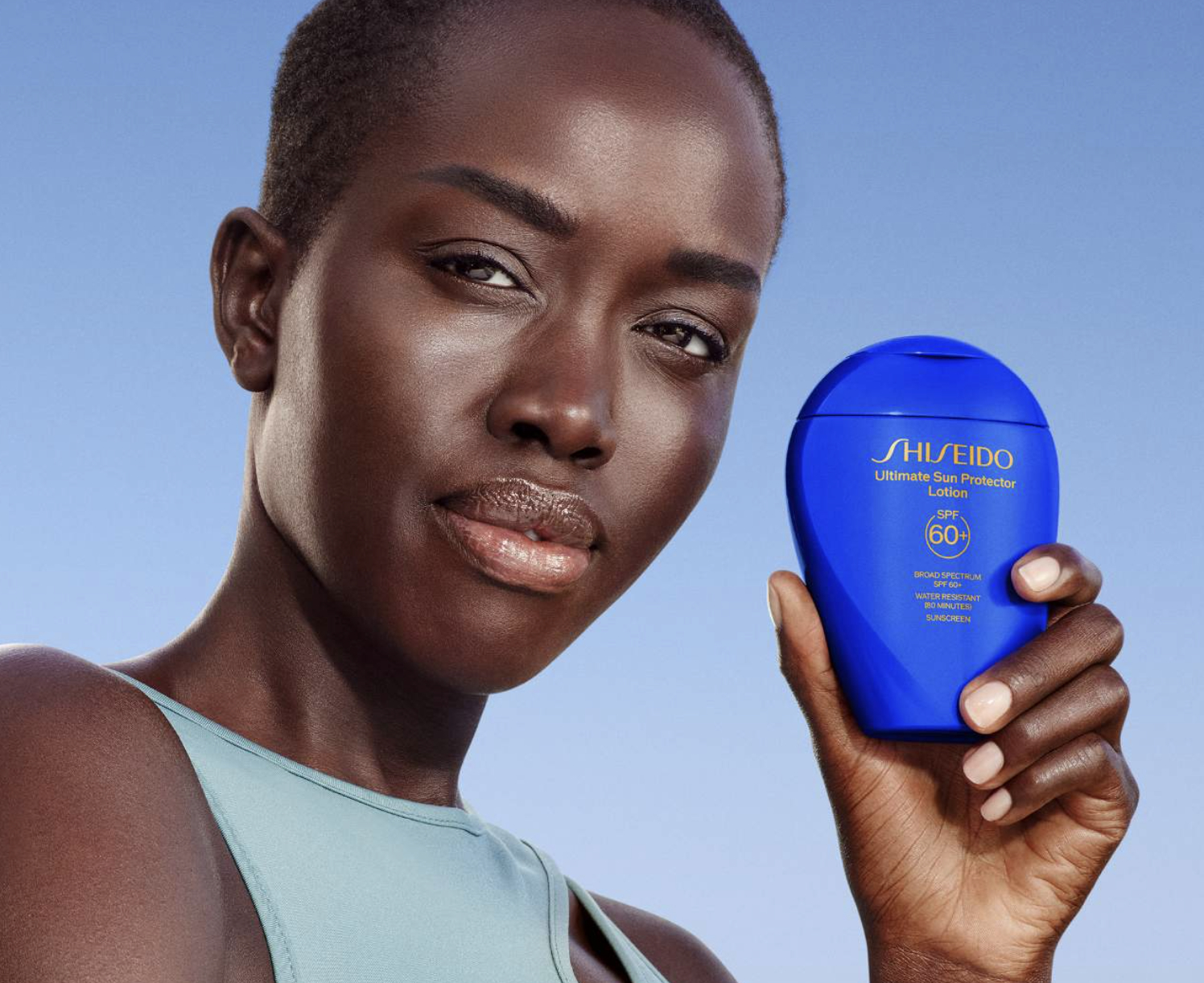 Woman holding Shiseido sunscreen product, looking at the camera, wearing a sleeveless top. Great for shopping skincare essentials