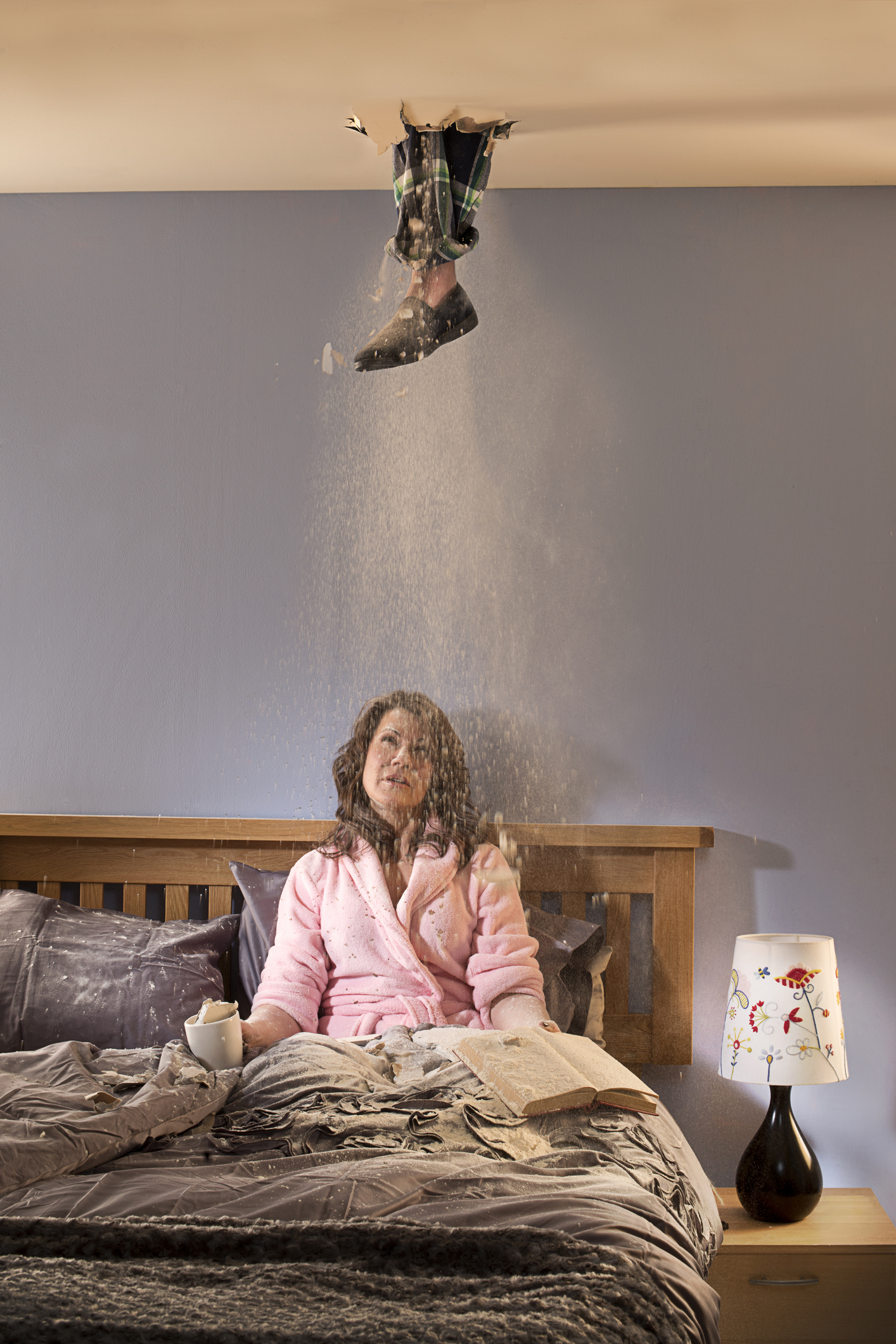 Person sitting in bed with a burst ceiling above, creating a dust explosion