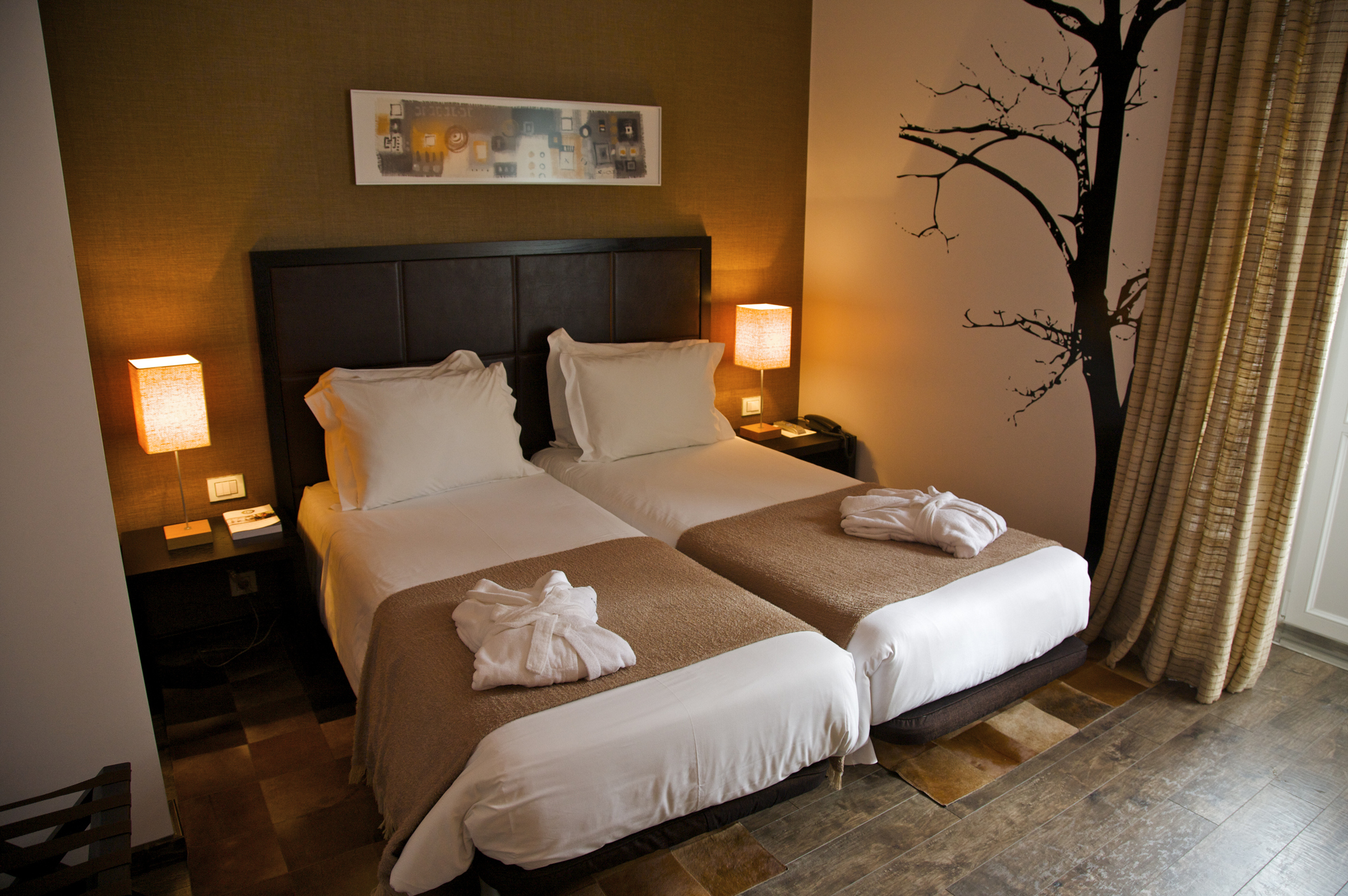 Hotel room with two beds pushed together, nightstands with lamps, and a decorative wall tree