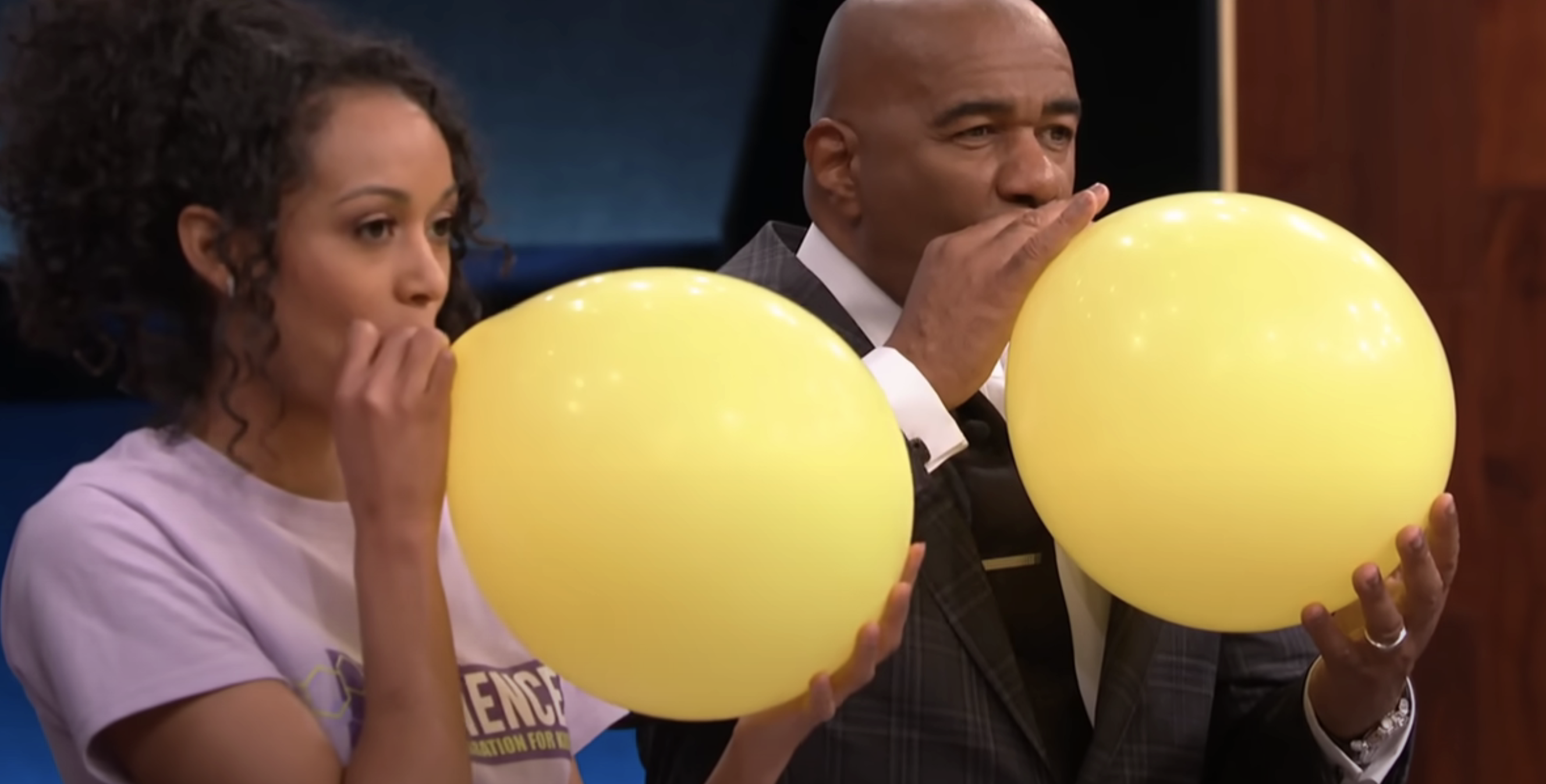 Two people holding large yellow balloons to their mouths, appearing to be inhaling from them