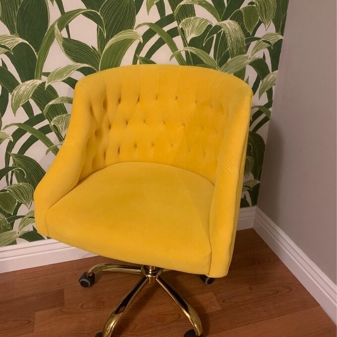 Yellow tufted office chair with gold base against a leaf-patterned wall