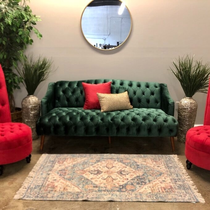 Green tufted sofa with two red chairs and decorative pillows in a styled living room setting