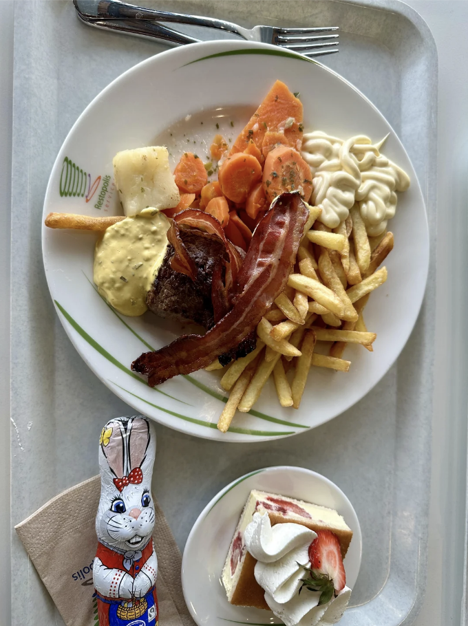 Plate with various foods including bacon, eggs, and fries, next to a chocolate bunny and a slice of strawberry cake