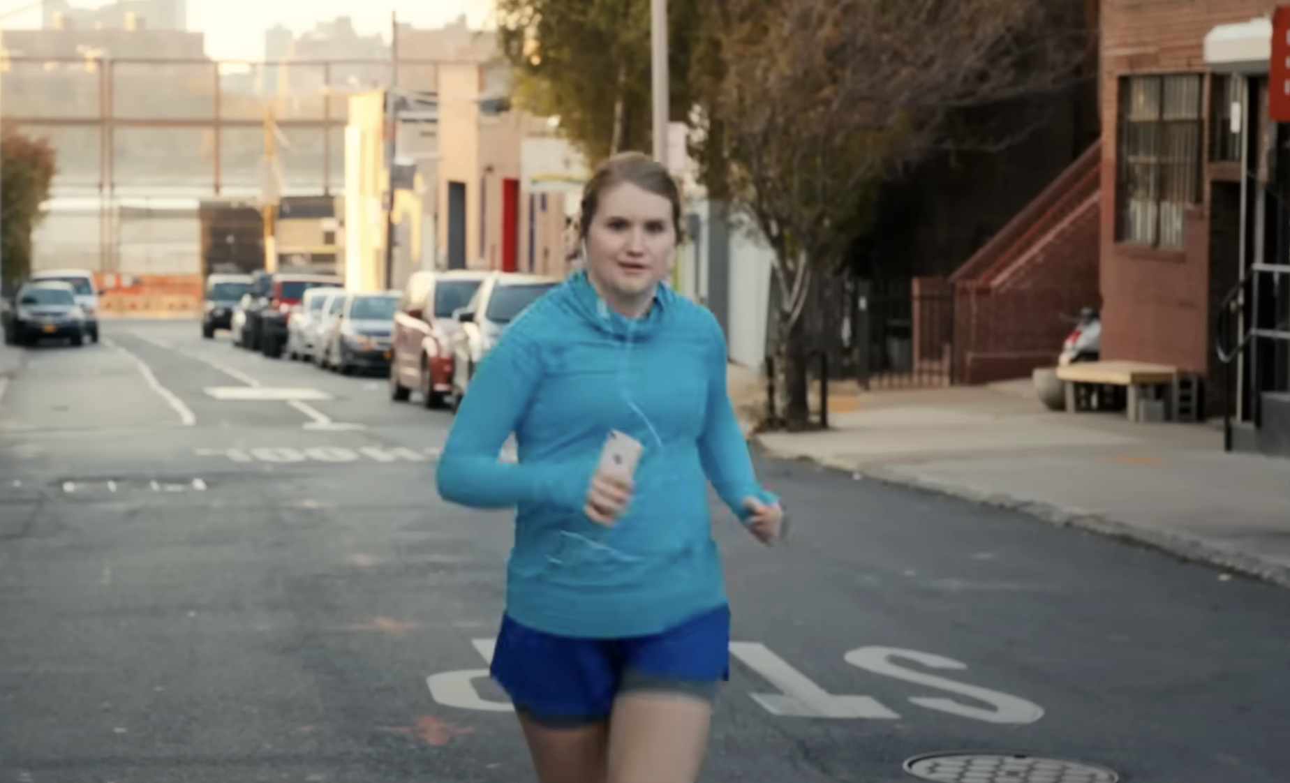Woman jogging on a city street with headphones, in athletic wear
