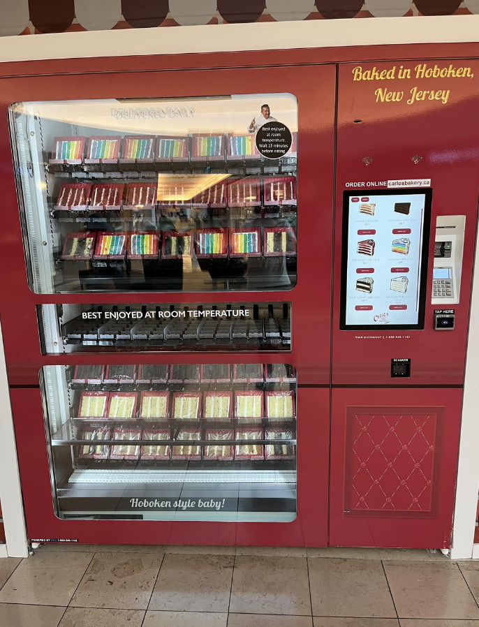 Vending machine stocked with various flavors of cake slices, labeled for ordering and pickup