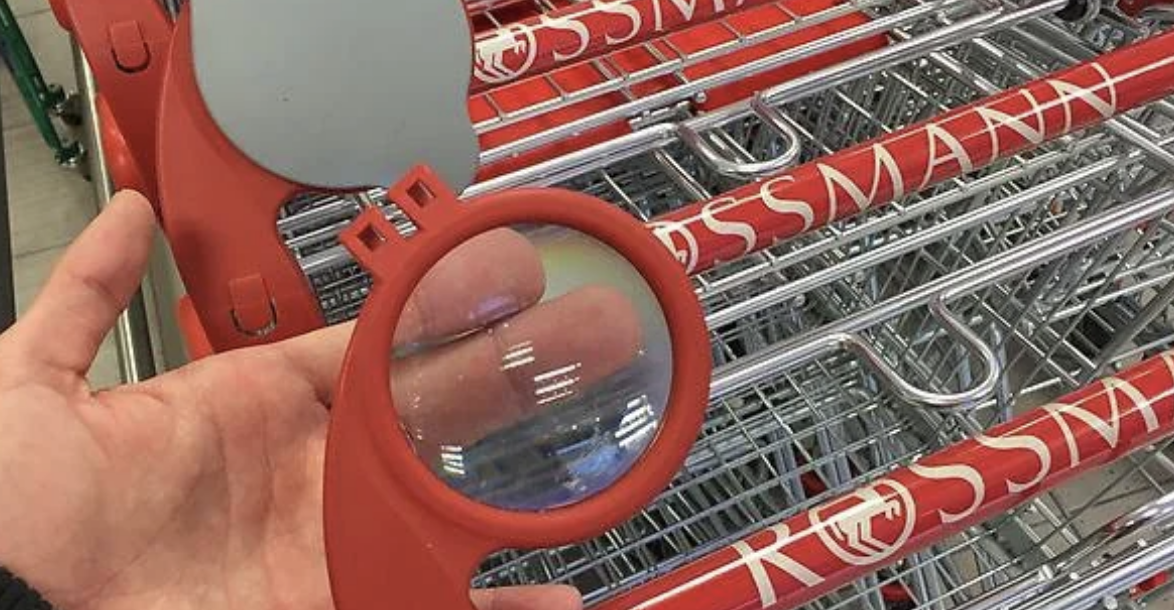 Person&#x27;s fingers seen through a magnifying glass attached to a shopping cart handle