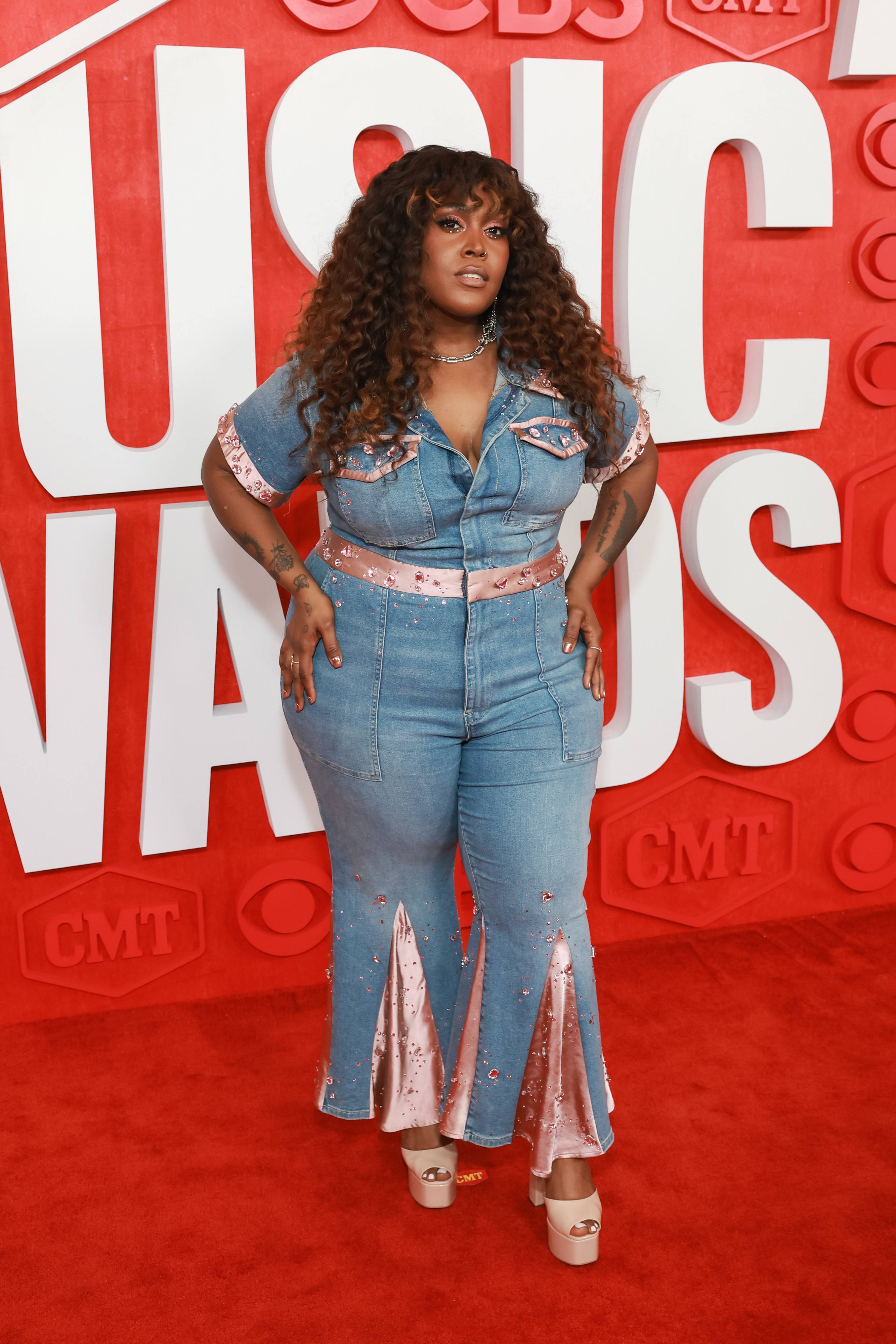Brittney Spencer stands on the red carpet in a denim outfit with sparkling accents and heels