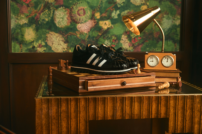 Black Adidas sneakers displayed on a wooden stand with vintage decor in the background