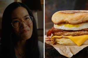 Woman with glasses smiling and a breakfast sandwich with egg, bacon, and cheese
