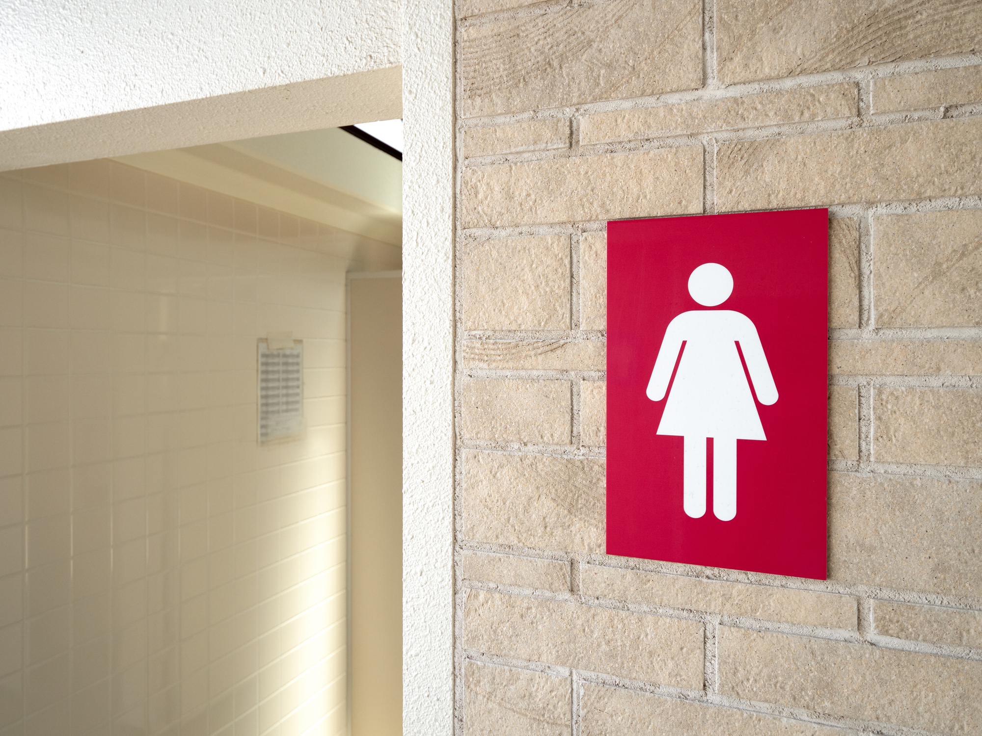Women&#x27;s restroom sign on a brick wall next to a bathroom entrance