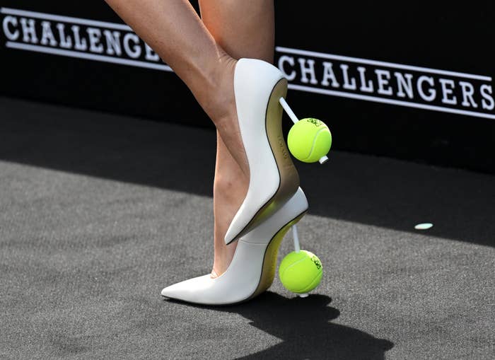 A person in high heels stands on a tennis ball at a sporting event