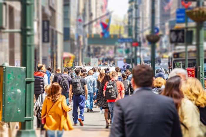 Crowd of people walking on a city street with vehicles and buildings in the background
