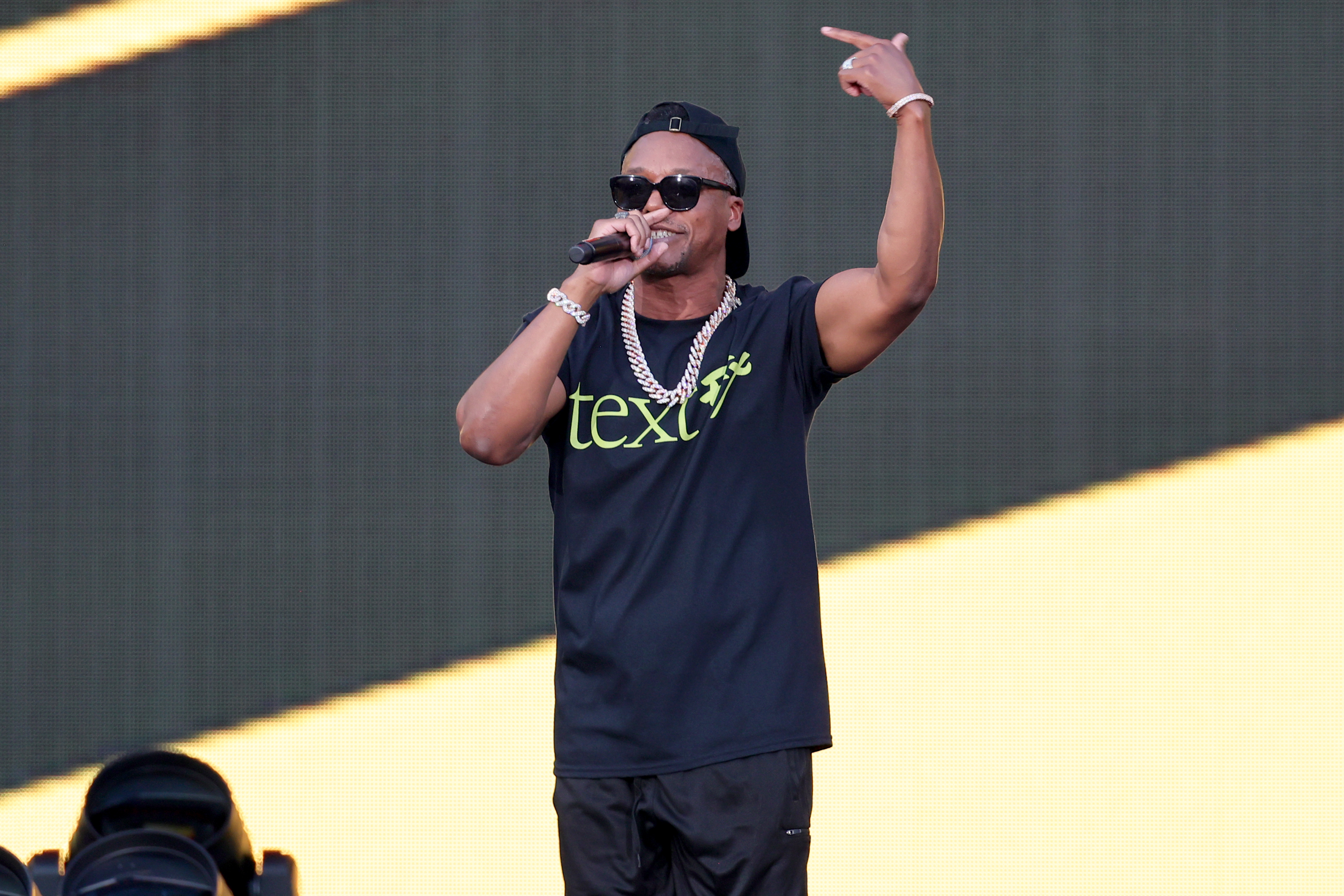 Music artist performing on stage with microphone, wearing casual attire and sunglasses
