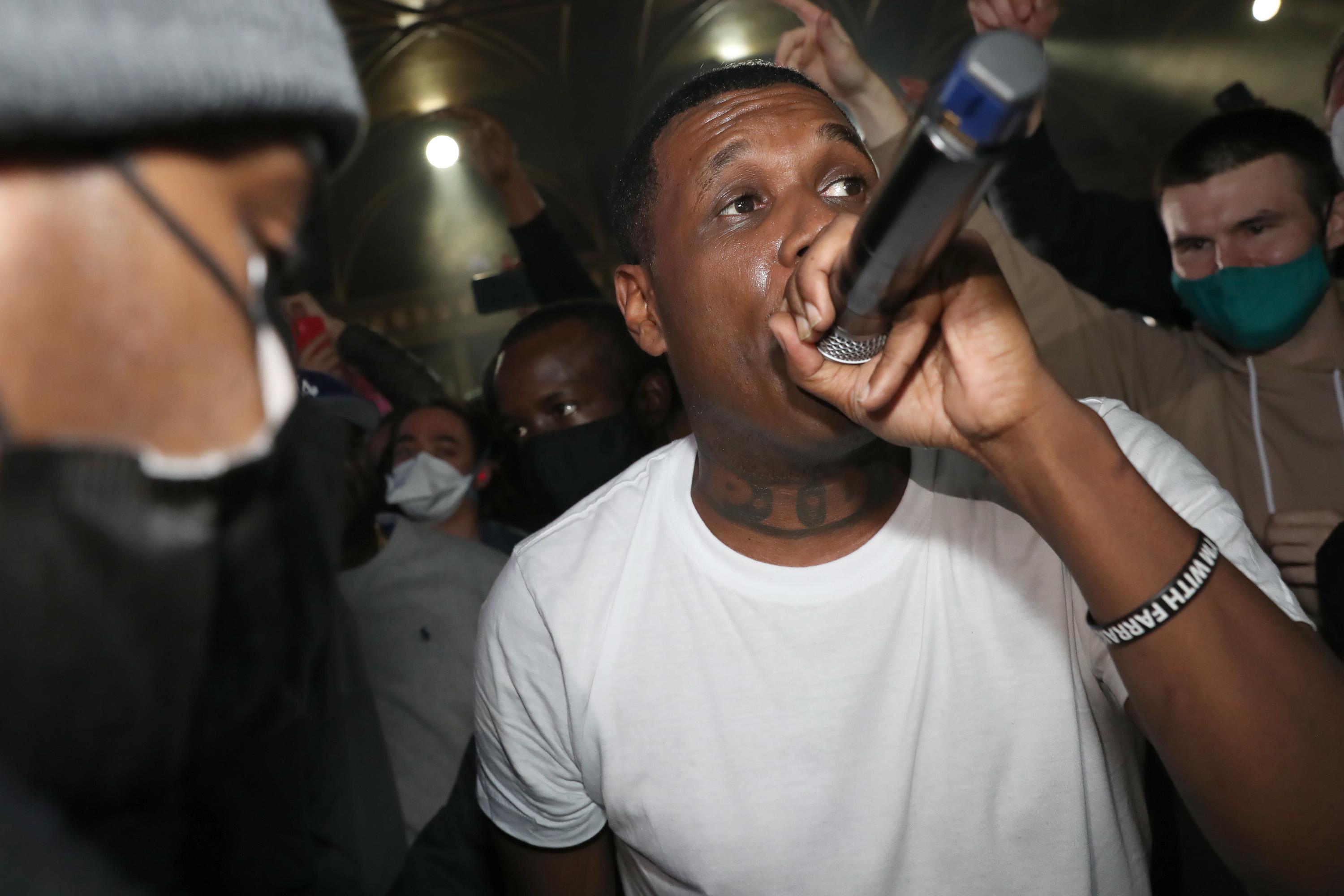 Rapper in a white tee performing with a mic, surrounded by an attentive crowd