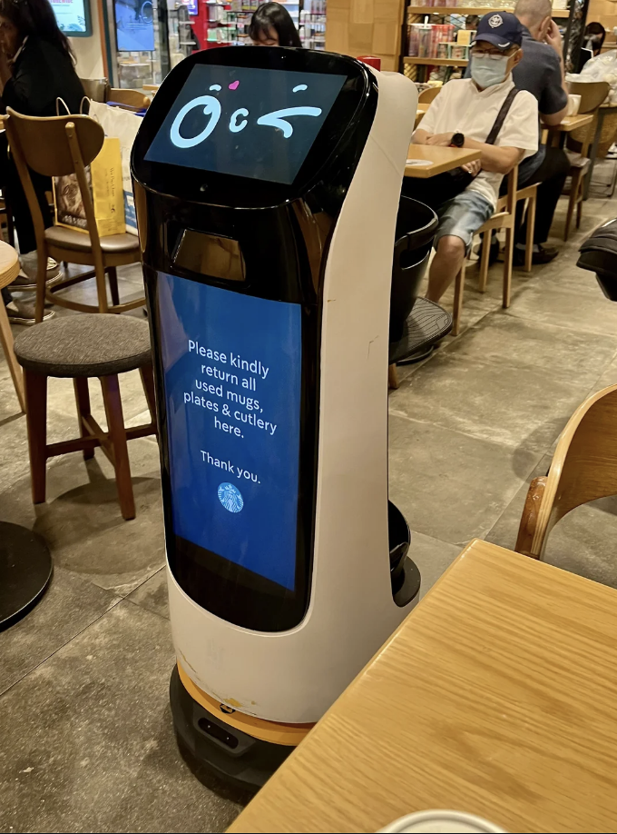 Service robot with a screen displaying a message to return used plates, cups, and cutlery, in a cafe setting