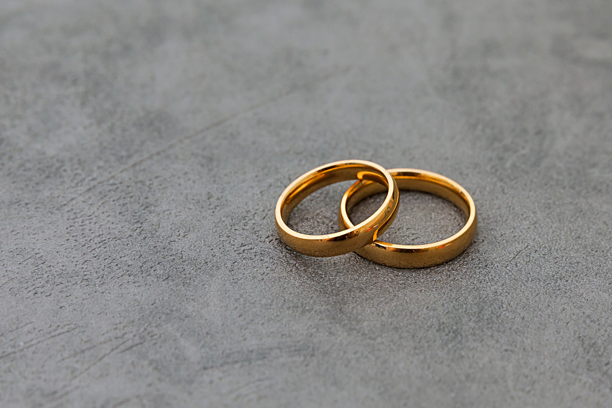 Two wedding bands intertwined on a textured surface
