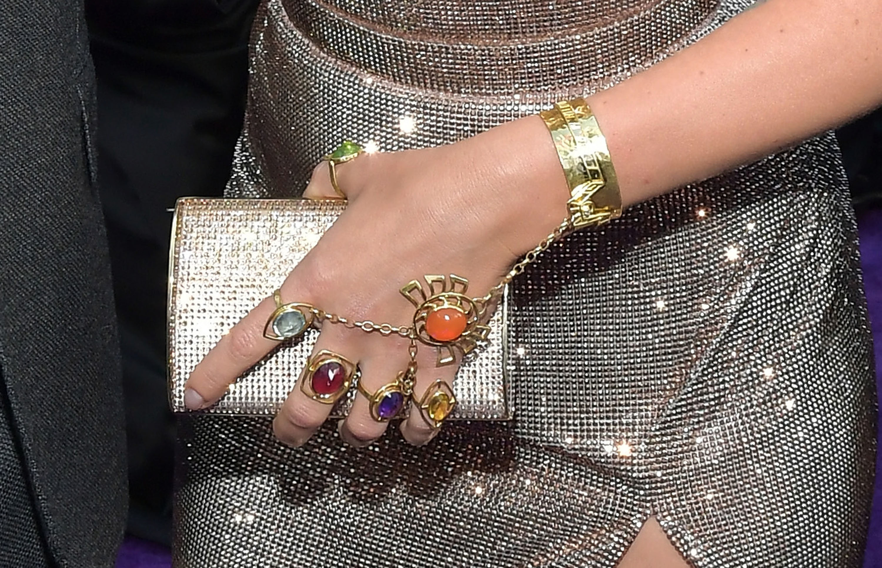 Close-up of a person&#x27;s adorned hand with a sparkling clutch, gold bracelet, and colorful rings
