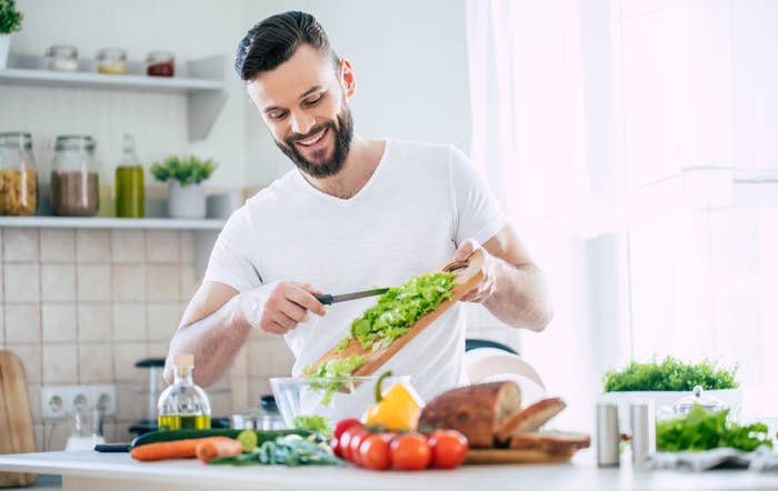 Man smiling while chopping vegetables in a bright kitchen setting
