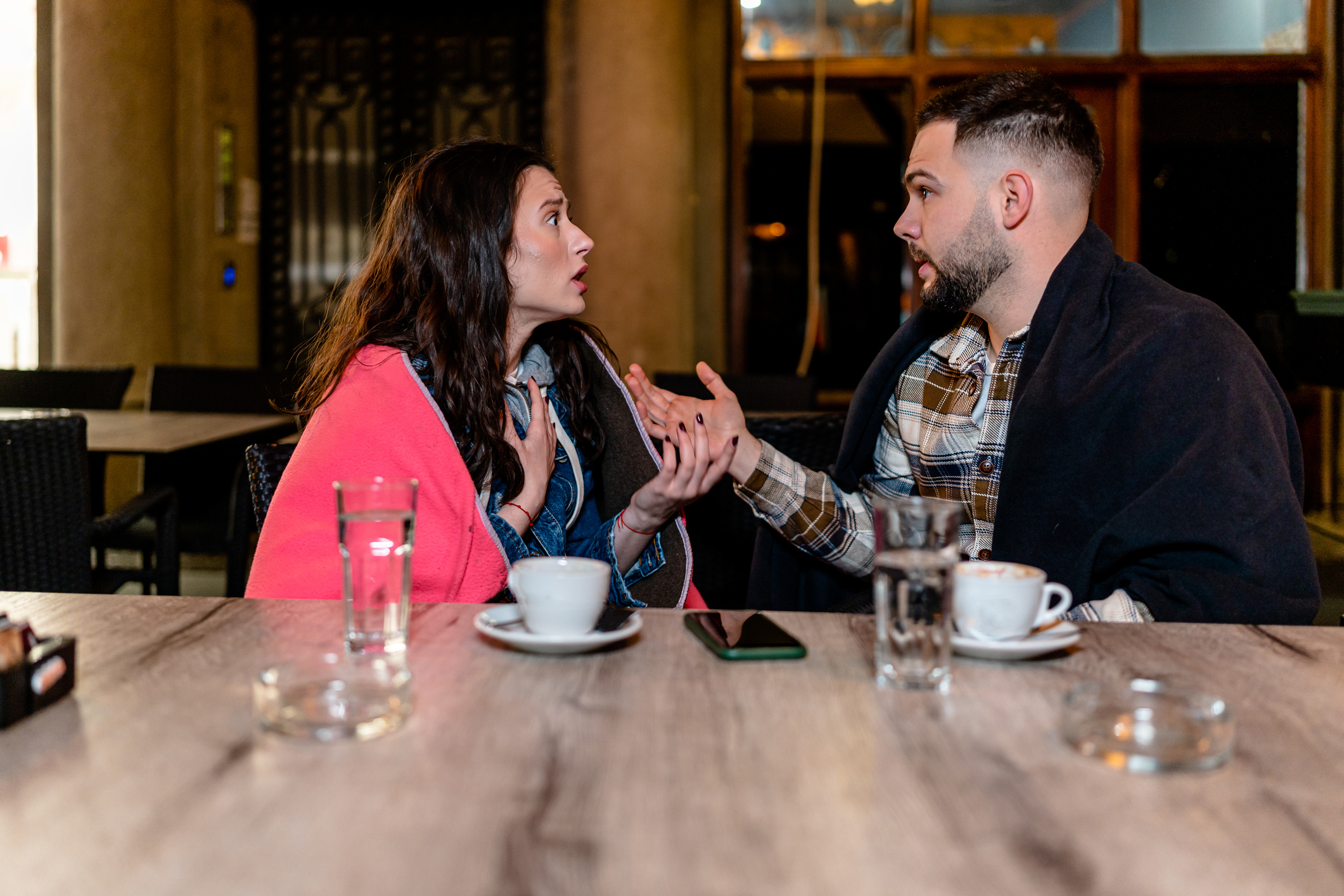Two people engaged in a conversation at a cafe table with drinks and a phone visible
