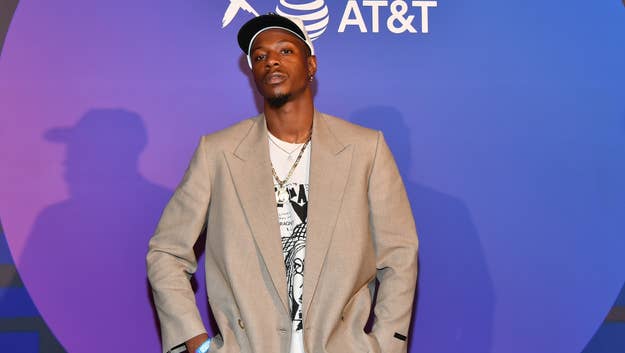 Person posing at event, wearing a beige suit jacket, graphic tee, and chain necklace