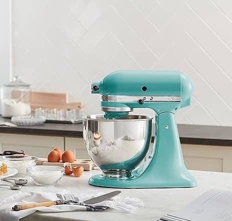Stand mixer on kitchen counter with ingredients and utensils around it; pie in foreground