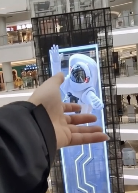 Person interacting with a 3D astronaut advertisement on a digital kiosk in a mall