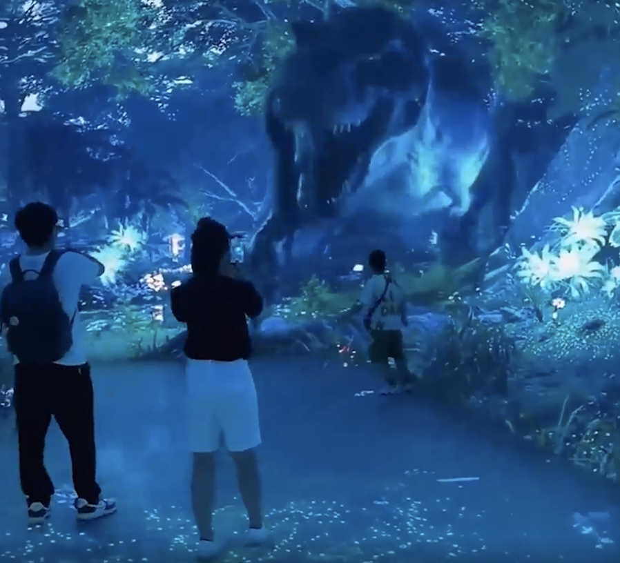 Visitors watch a projected dinosaur in a dark, immersive exhibition space