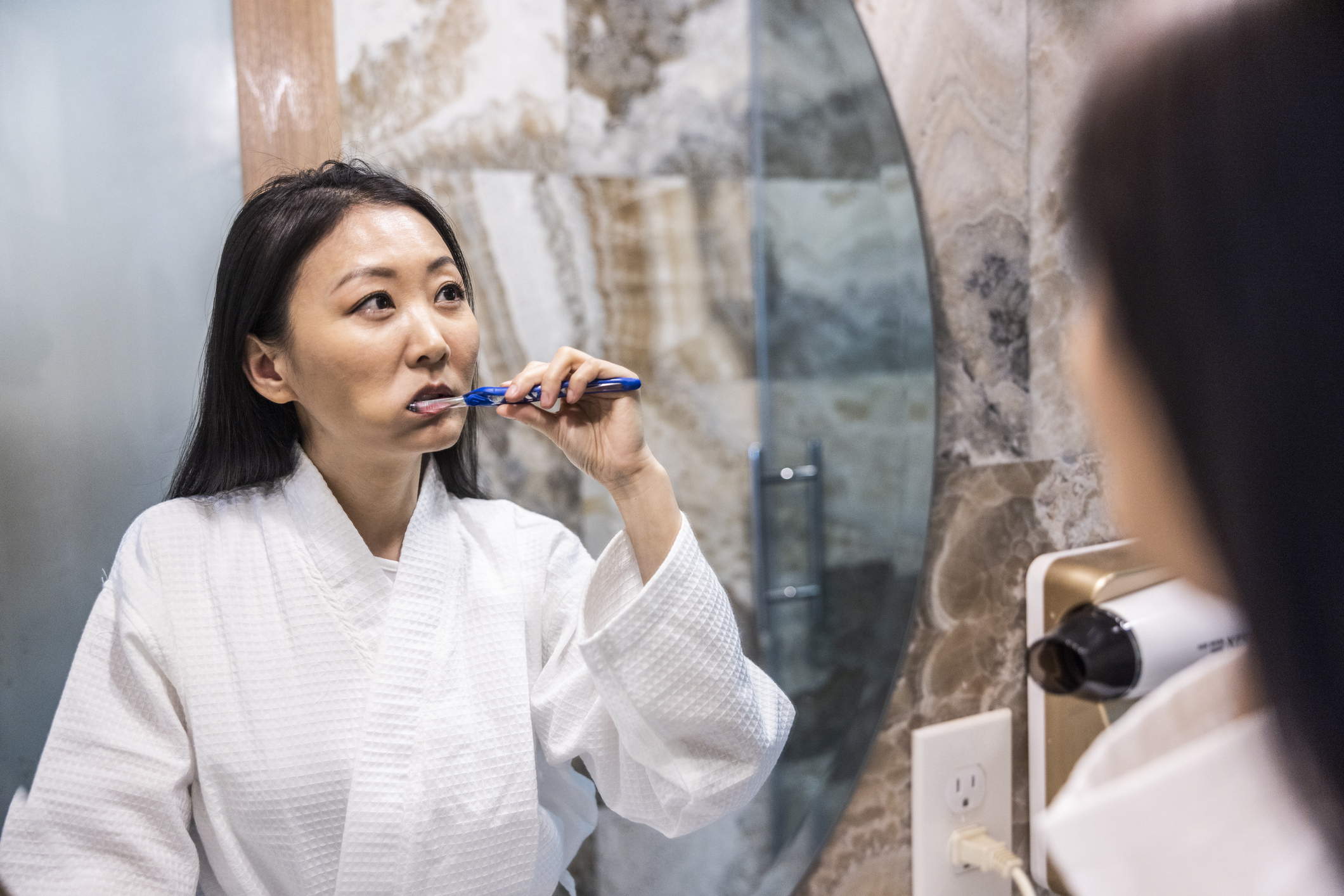 Person in a robe brushing their teeth in front of a mirror