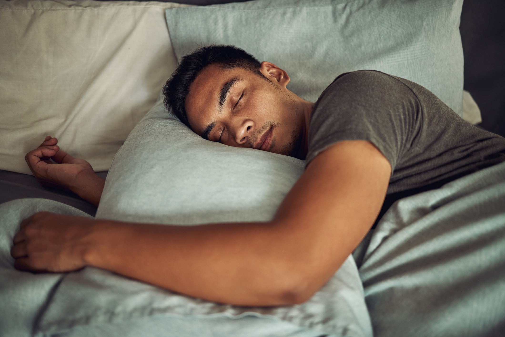 Man resting with eyes closed, hugging a pillow on a bed