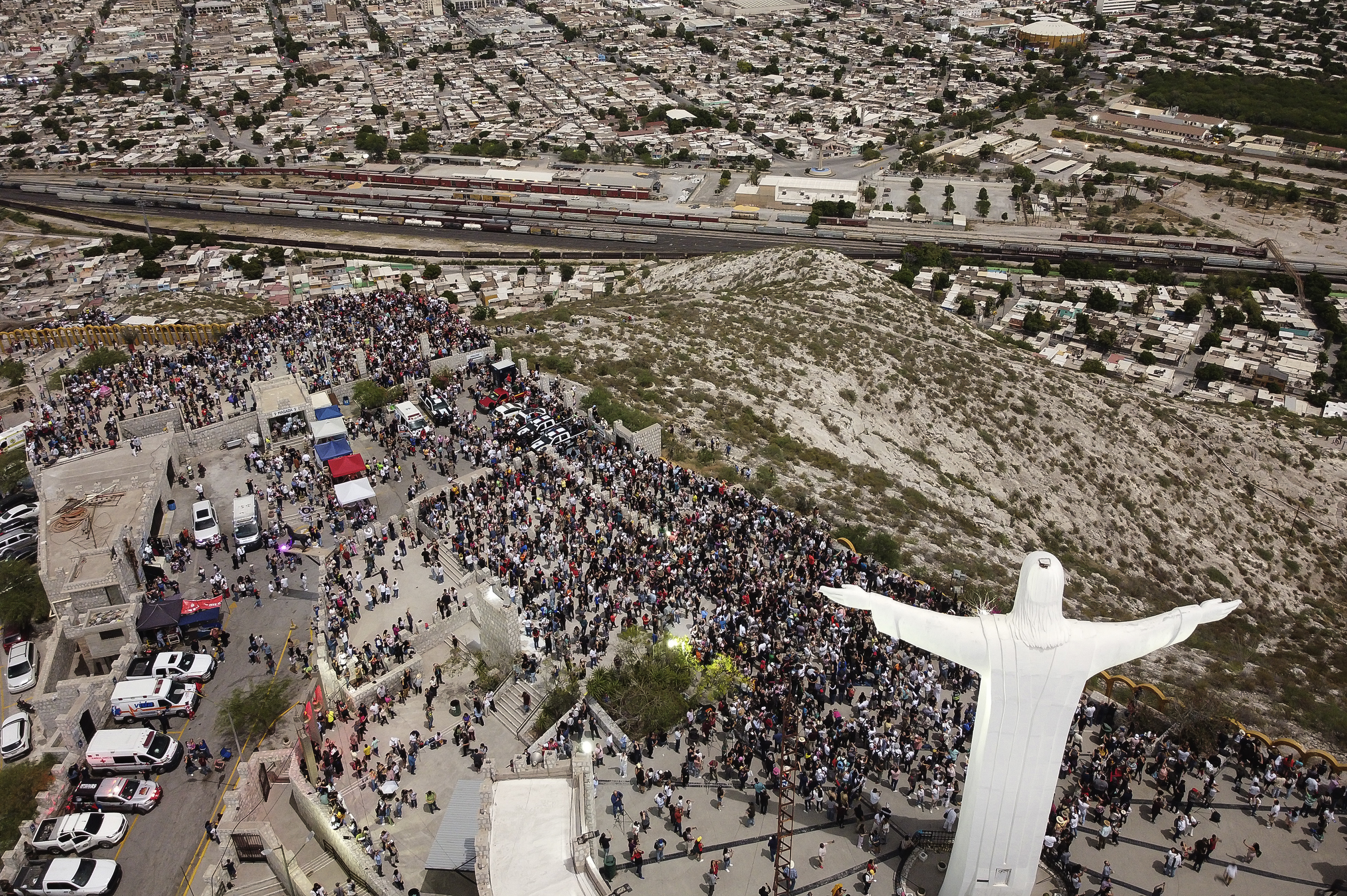 Aerial view of a large crowd gathered around a statue of Jesus with outstretched arms on a hilltop