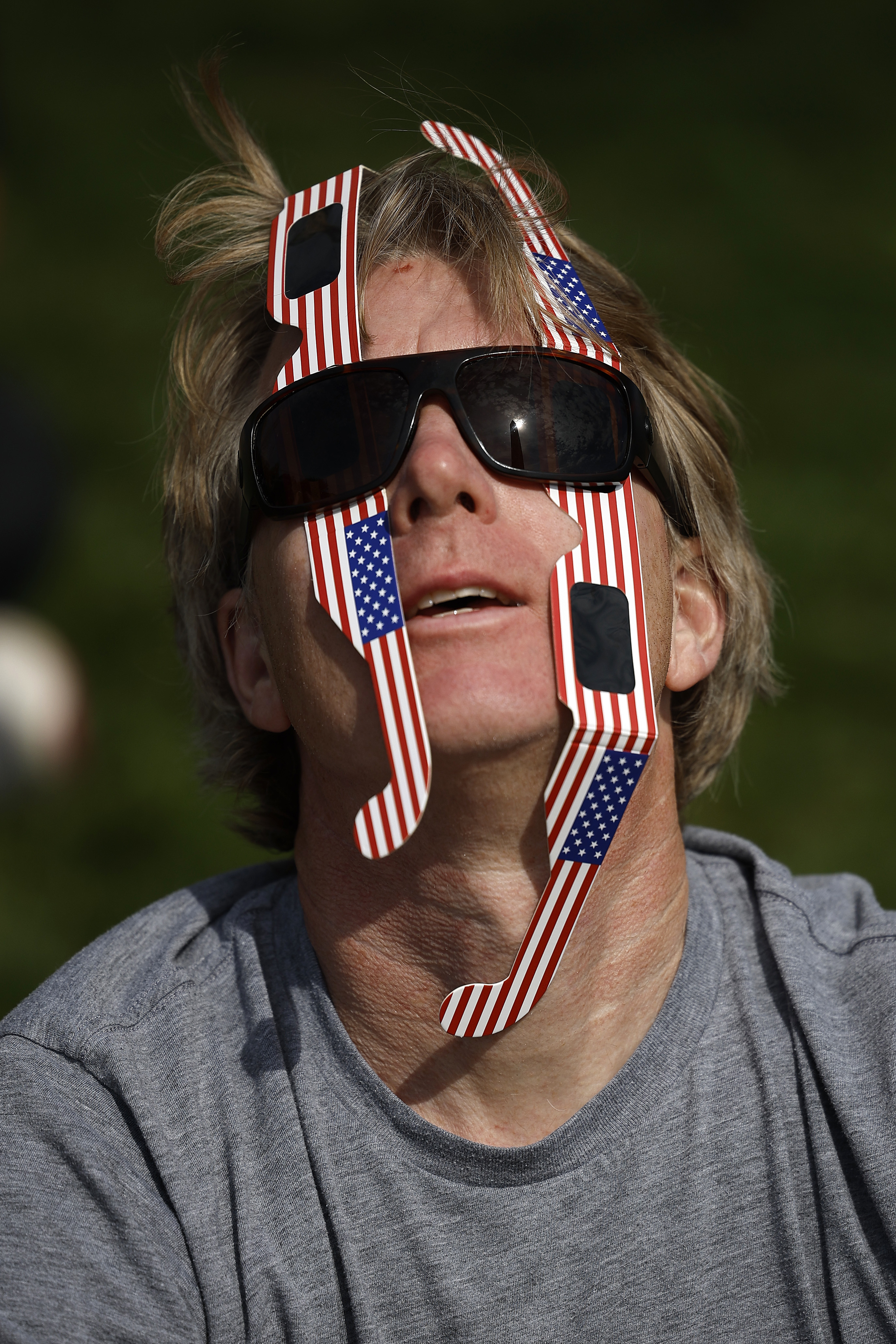 Person wearing sunglasses and patriotic ribbon, looking upward with an open mouth
