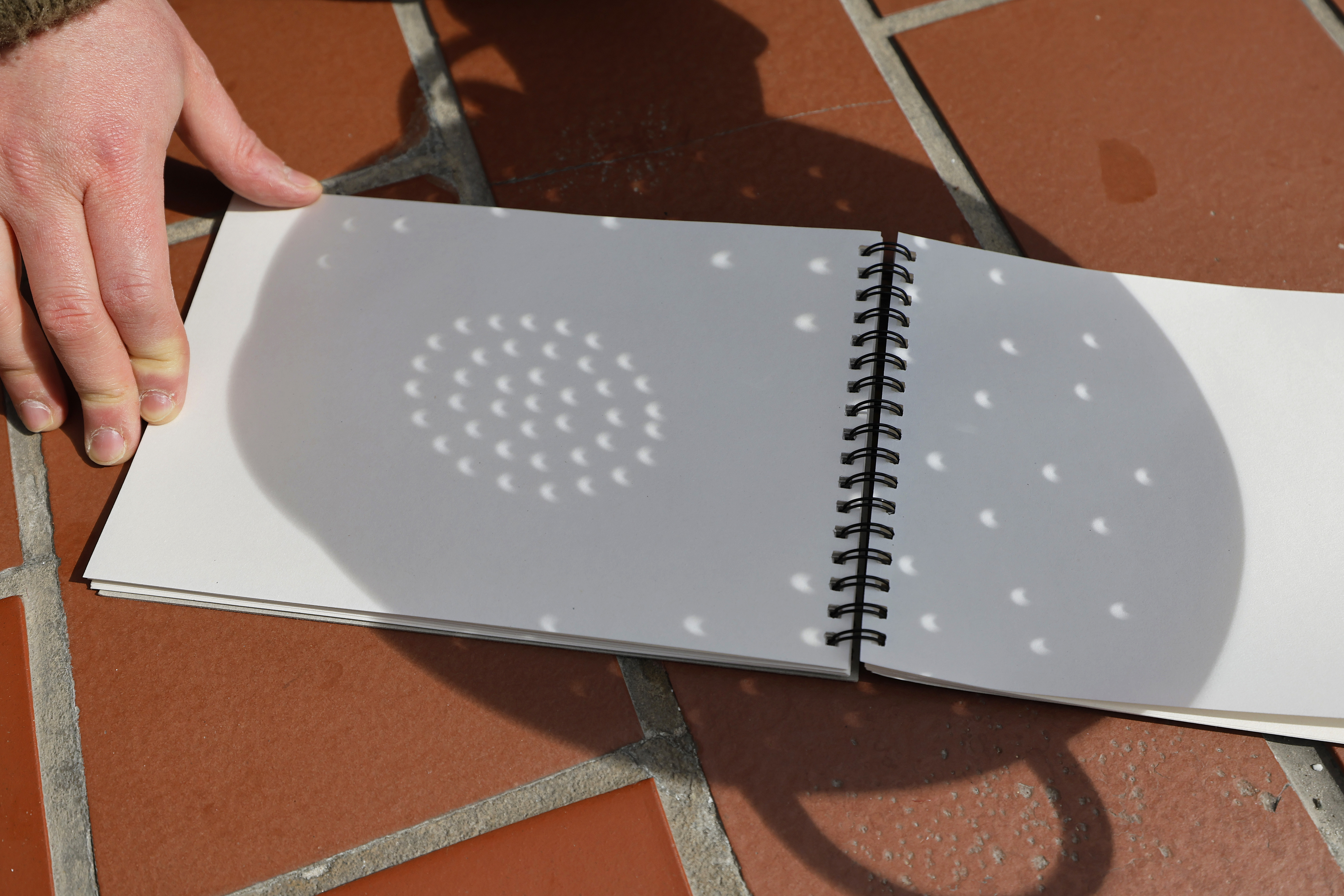 Hand holding a notebook with a shadow pattern cast on open blank pages