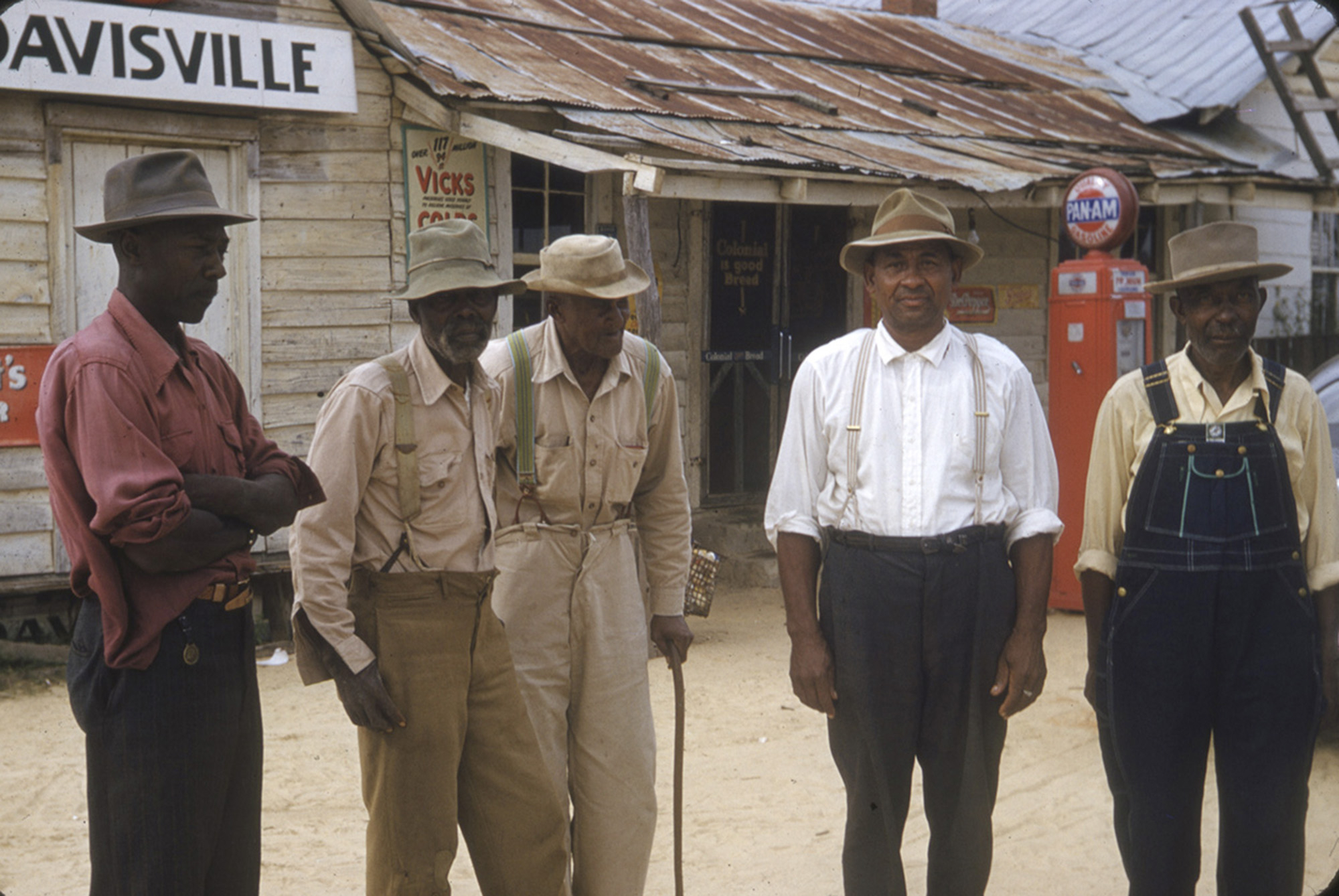 Group of five men in vintage workwear standing in front of a rustic wooden building