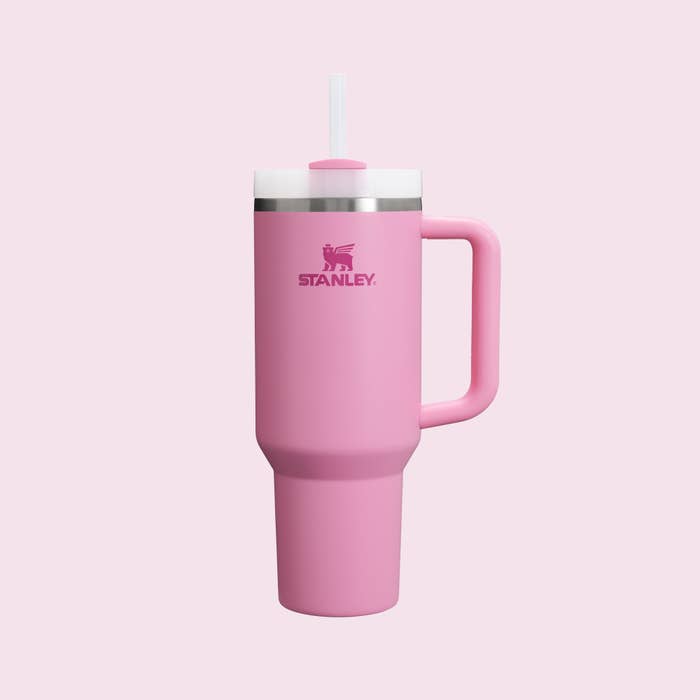 Stanley brand pink insulated travel mug with handle and straw on a plain background