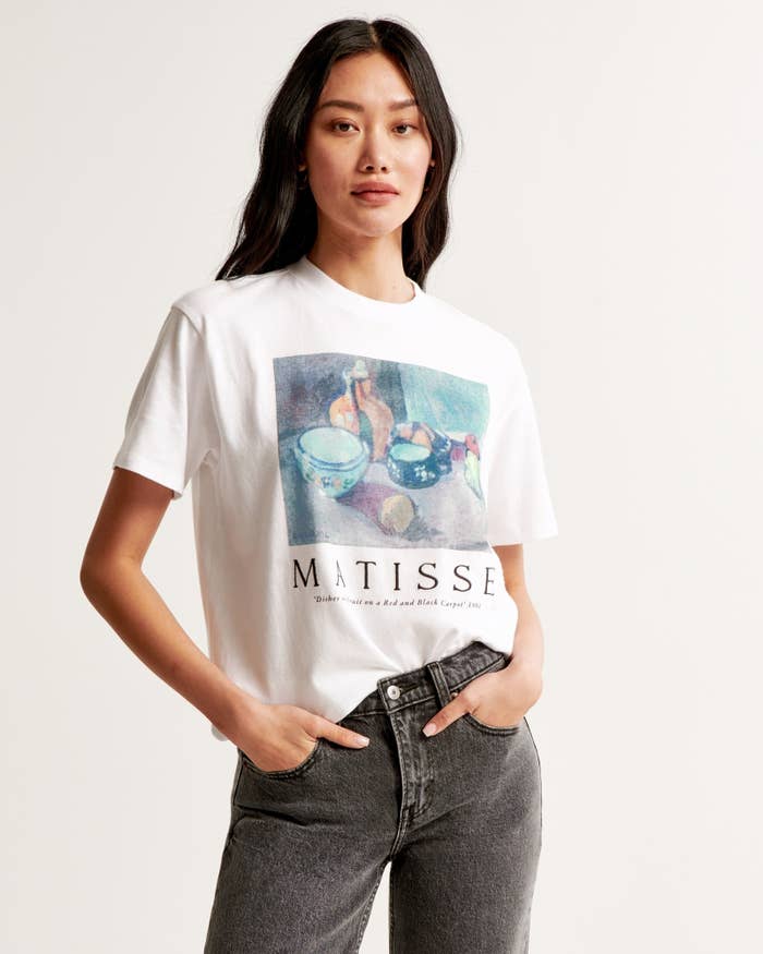 model in a white tee with Matisse print, paired with grey jeans, hands on hip