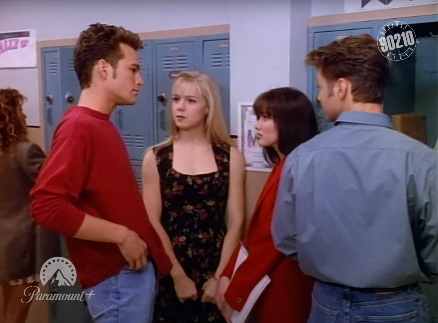 Four characters from Beverly Hills, 90210 stand by lockers, displaying a tense interaction