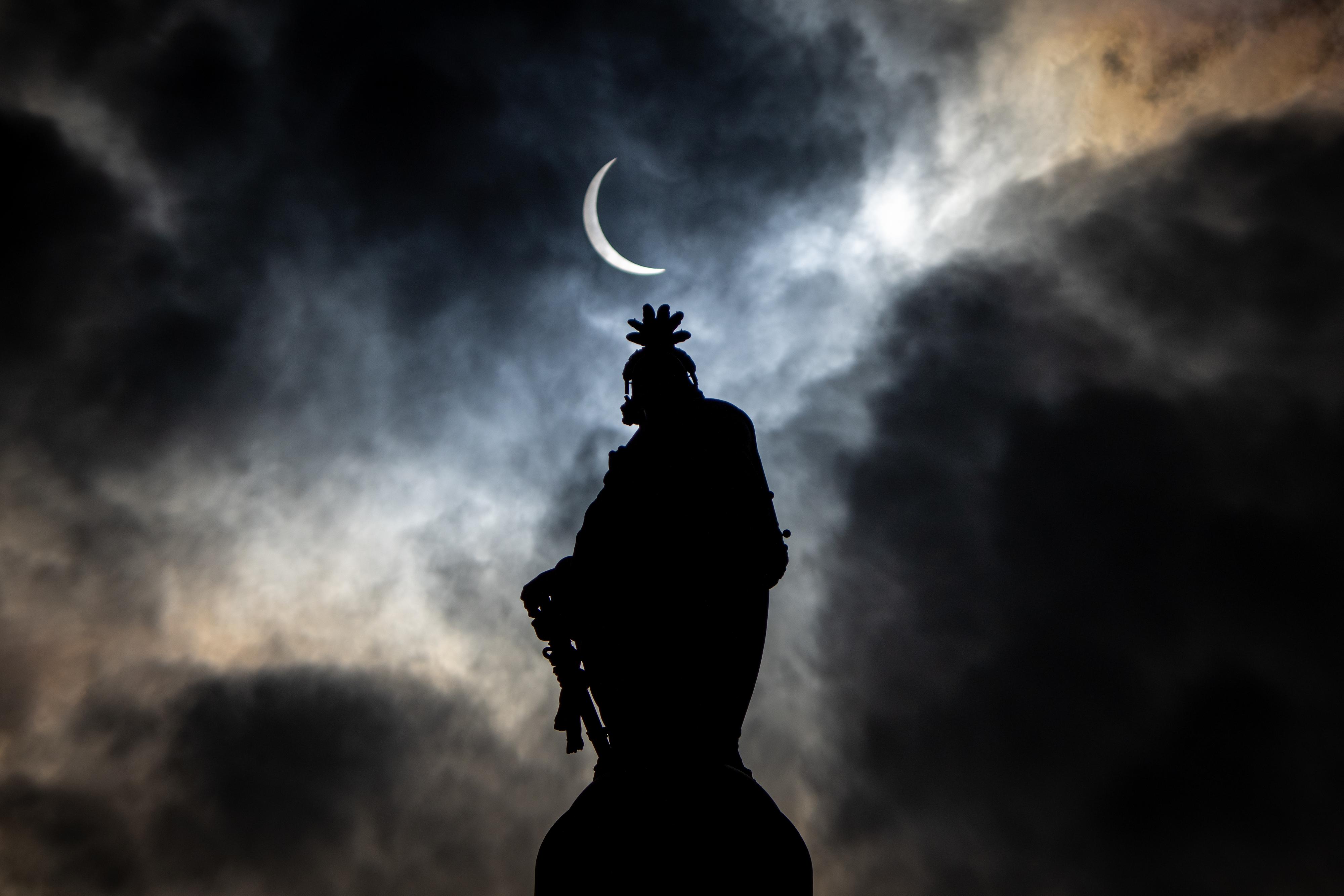 Silhouette of a statue against the night sky with a crescent moon above