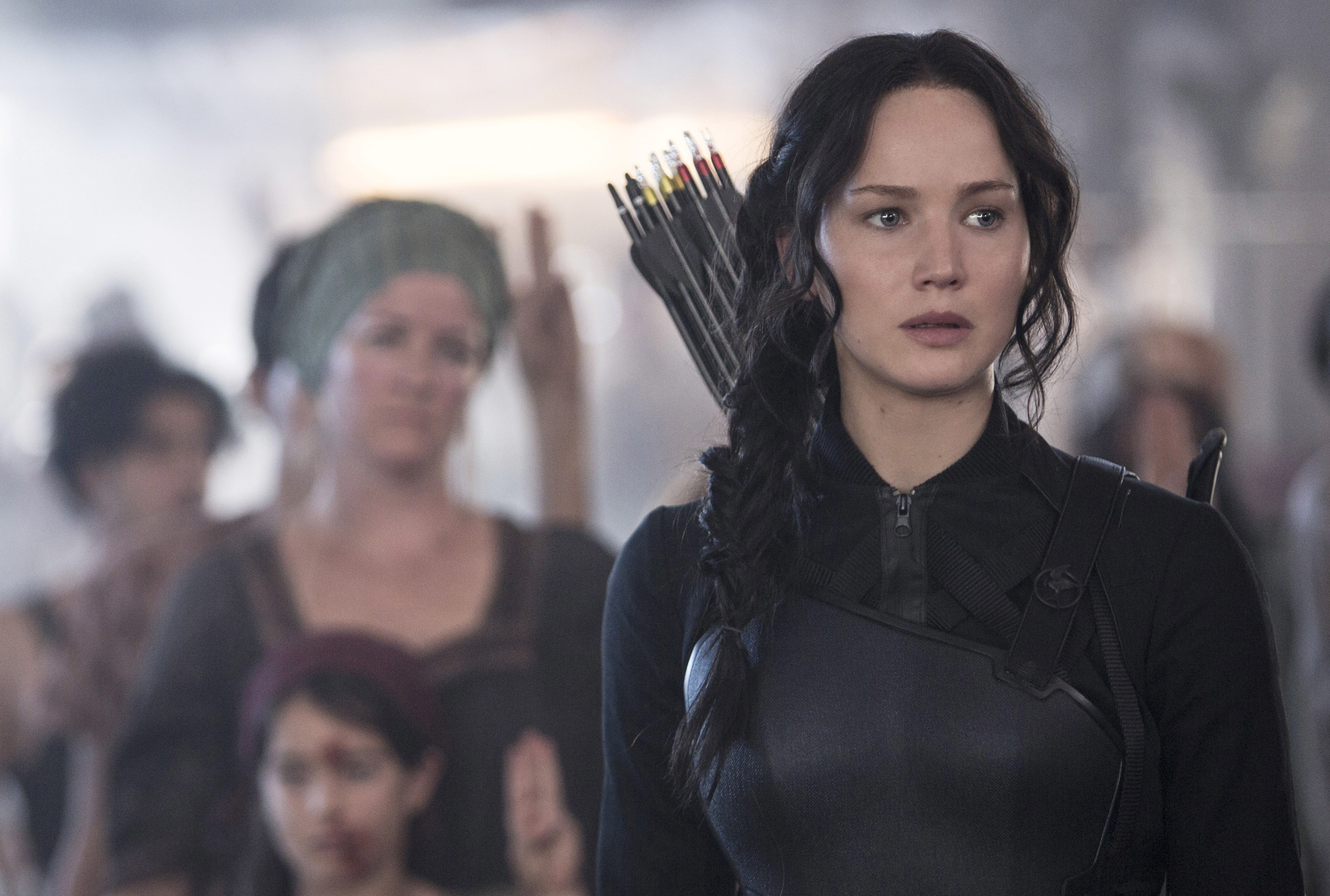 Katniss Everdeen in a dark combat outfit with a quiver of arrows on her back, standing in a crowd